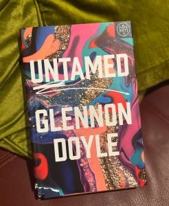 The book, Untamed by Glennon Doyle, lying on a leather couch with throw pillows.