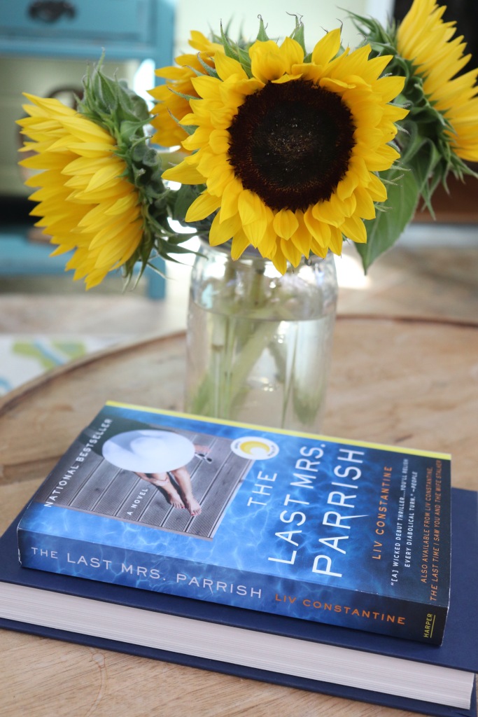 The Last Mrs. Parrish sitting on a round wood table in front of sunflowers in a mason jar vase.
