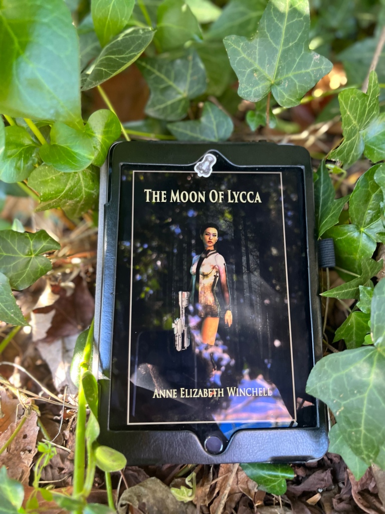 The cover of The Moon of Lycca displayed on an e-reader. The e-readers is surrounded by green ivy.